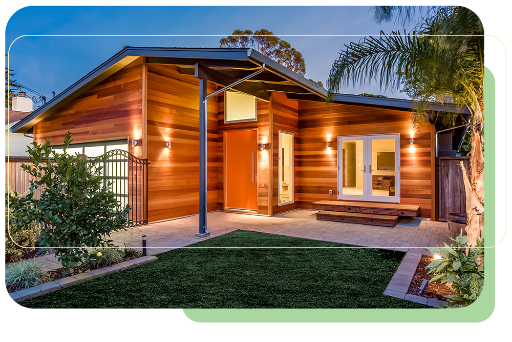 beautiful contemporary home exterior at night lit up by sconces on the cedar siding with lush landscaping in the yard